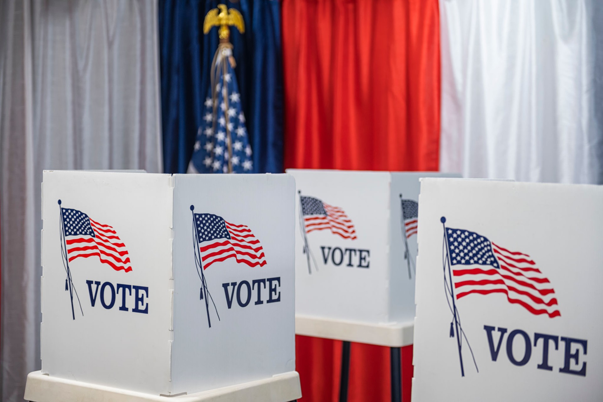 Three empty voting booths with bunting and American flag